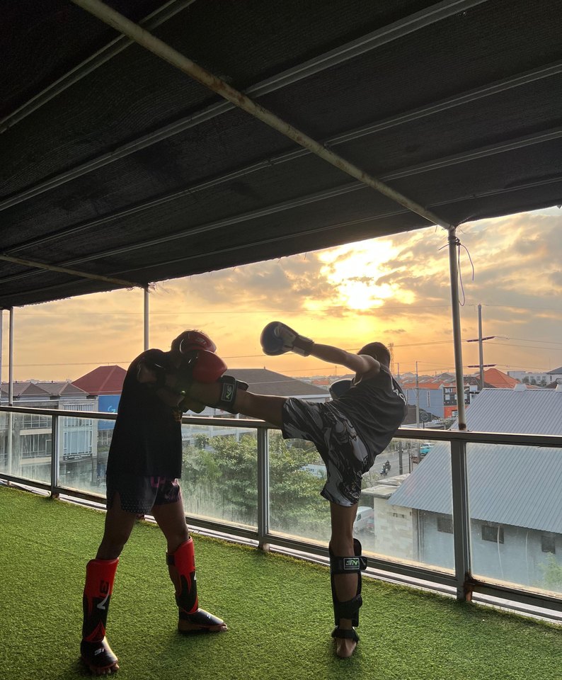Muay Thai fighter landing a high kick on the open-air rooftop mat at sunset
