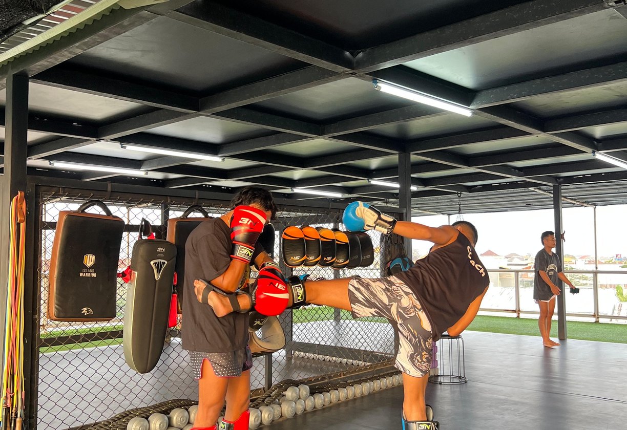 Fighter landing a high kick on Thai pads inside the open-air rooftop cage at Island Warrior Bali