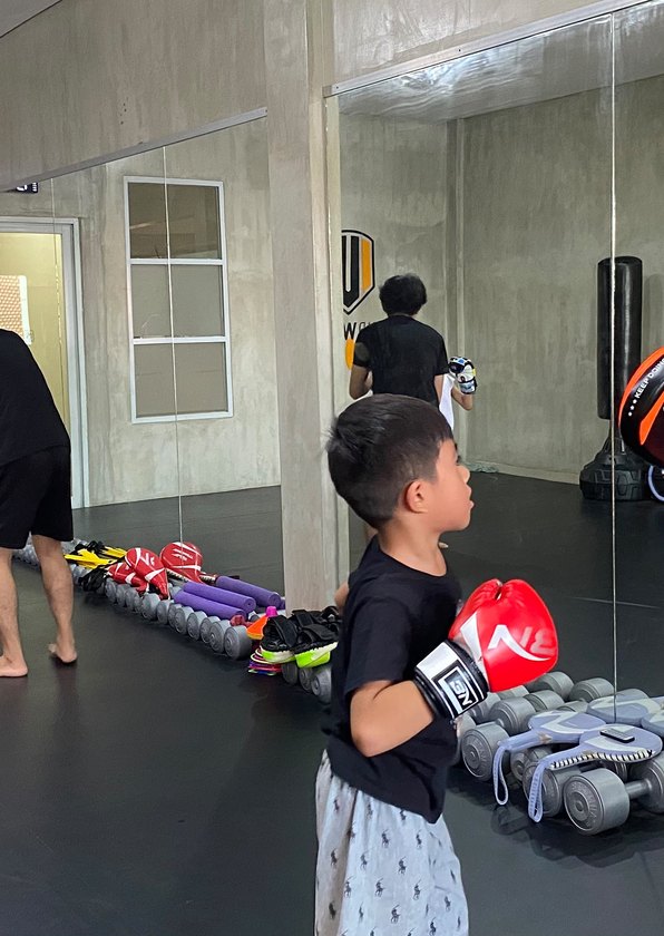 Young student in red boxing gloves training in front of the mirror wall during a kids class