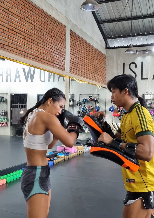 Coach in a yellow jersey holding orange kick pads for a student in the Island Warrior Bali training hall