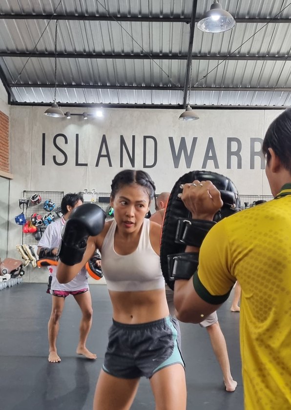 Muay Thai student in a white top punching into focus mitts under the Island Warrior wall graphic